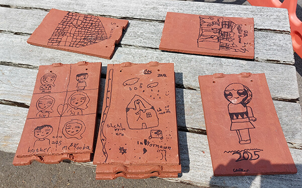 A selection of clay tiles decorated by the school pupils depicting a house, family members and cartoon characters